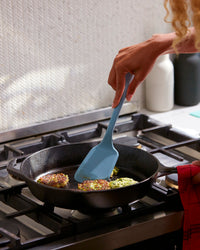 A hand holding the GIR Ultimate Light Blue Flip to flip patties on a frying pan.