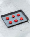 The Half Sheet Slate Baking Mat with Red Macaroons on it.