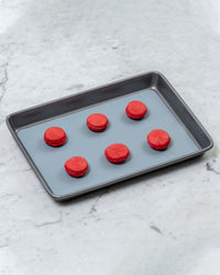 The Half Sheet Slate Baking Mat with Red Macaroons on it.