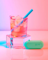 A GIR Kids Straw in a glass of juice with ice on a pink background.