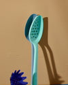 The Teal Perforated spoon and Light Blue Ultimate Spoon, standing upright on a yellowish background