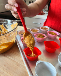 Cupcake batter being poured into the Strawberry Swirl Cupcake Liners using a Red Ultimate Spatula placed on a baking tray.