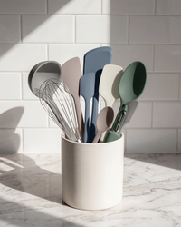 Set of colorful kitchen utensils in a white holder against a tiled wall.
