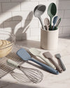 Set of colorful kitchen utensils including spatulas and a whisk on a marble countertop with a tiled wall background.