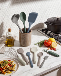 Set of kitchen utensils including spatulas, spoons, and a whisk on a kitchen counter with ingredients.