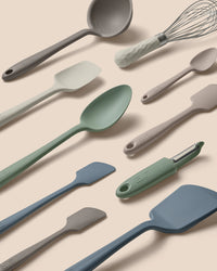 Set of kitchen utensils including spatulas, ladle, and whisk on a beige background