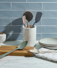 Kitchen utensils in a holder on a countertop with a blue tiled wall background