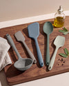Set of silicone kitchen utensils on a wooden cutting board with a bottle of oil and herbs.