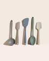 Set of five kitchen utensils including ladles and spatulas in various colors on a beige background