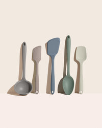 Set of five kitchen utensils including ladles and spatulas in various colors on a beige background