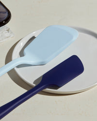 Close up of the GIR Navy Ultimate Spatula and Light Blue Ultimate Flip on a white plate. 