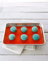 The Half Sheet Red Baking Mat with Teal Macaroons on it. 