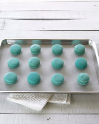 The Studio 12 x 17 Baking mat on a tray with teal macaroons on it. 