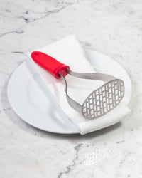 The GIR Perforated Masher in red on a white towel and plate. 