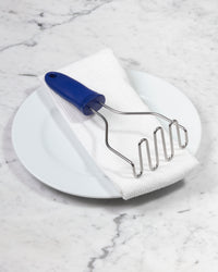 The GIR Wired Masher in Royal Blue on a white towel and plate.  