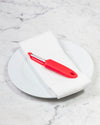 The I Handle Flat Peeler in Red on a white towel and plate. 