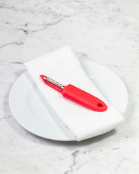 The I Handle Serrated Peeler in Red on a cream background. 