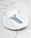  The Y Handle Flat Peeler in Slate on a white towel and plate. 