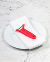 The Y Handle Julienne Peeler in Red on a white towel and plate.