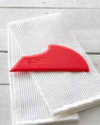 The GIR Scraper in Red resting on a white towels. 