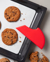 The GIR Scraper in red resting on a tray of cookies. 
