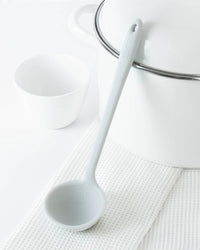 The Studio Skinny Ladle resting on a white towel on a white background.