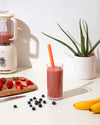 A Smoothie & Boba Straw in Super inside a smoothie on a white background with fruits and other kitchen equipment around it. 