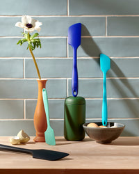 Different colored and sized GIR Spatulas displayed on a wooden counter with a blue background. 