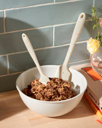 The Sprinkle Mini Spatula and Ultimate Spatula in a bowl of batter on a wooden surface. 