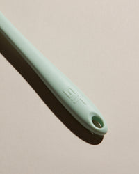 A close up of the Mint Spoonula Handle on a cream background. 