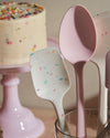 The Sprinkle Ultimate Spoonula in a cutlery holder with other GIR tools and a cake in the background. 