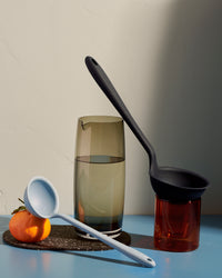 Two GIR Ladles one resting on two glasses and one on an orange on a cream background. 