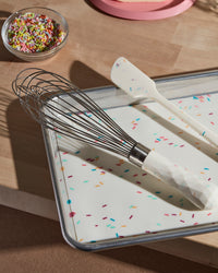 The Sprinkles Whisk resting on the Sprinkles Baking Mat next to the Sprinkles Spatula. 