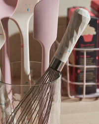 Close up of the Sprinkles Whisk on a glass holder with other GIR tools. 