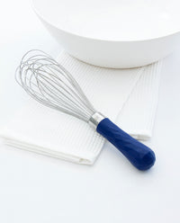 The Vincent Ultimate Whisk resting on a white kitchen towel next to a white bowl.