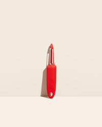 The I Handle Serrated Peeler in Red on a cream background. 