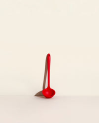 The Red Skinny Ladle on a cream background. 