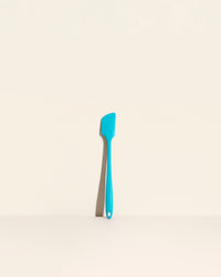 The Teal Skinny Spatula on a cream background. 