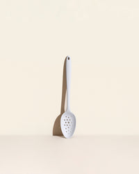 The Studio Perforated Spoon on a cream background. 