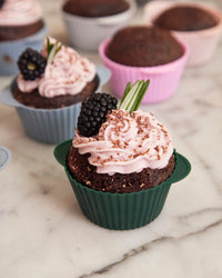  Close up of a baked chocolate cupcakes with icing and a blueberry on the Frosty Mint Cupcake liner. 