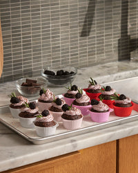 Baked chocolate cupcakes with icing and a blueberry on the Strawberry Swirl Cupcake liners on a kitchen counter. 
