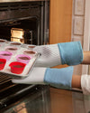 Hands wearing the Slate Oven Mitts on putting in a tray of cupcakes into the oven. 