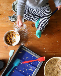 Toddler sprinkling ingredients on baking table with GIR 8 Piece Mini Bundle. 